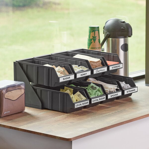 A black 2-tier Choice self-serve organizer with bins on a kitchen counter.