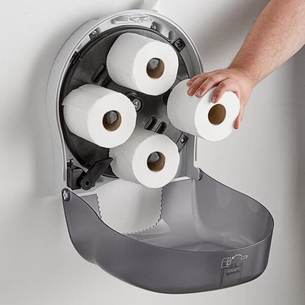 A hand holding a roll of toilet paper in front of a San Jamar Four Station Standard Roll Carousel Toilet Paper Dispenser.