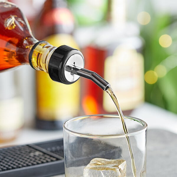 A person using a Choice chrome whiskey pourer to pour a drink into a glass.