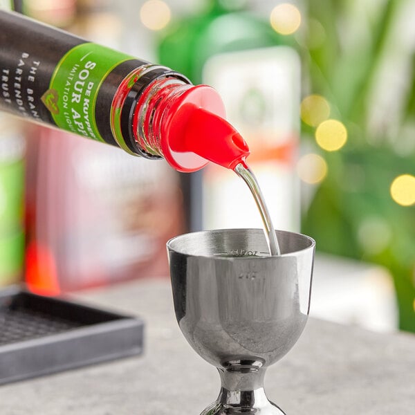 A bottle of red liquid pouring into a silver cup using a Choice red free flow liquor pourer.