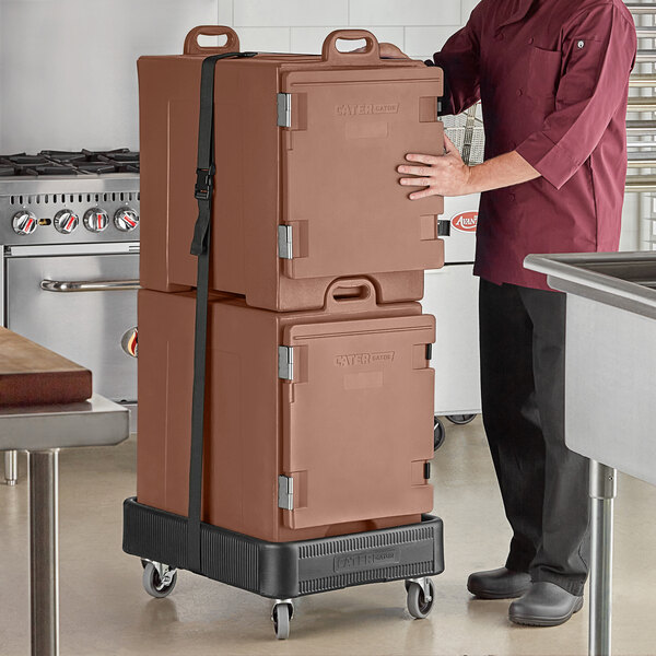 A chef in a brown uniform holding two large brown CaterGator insulated pan carriers.