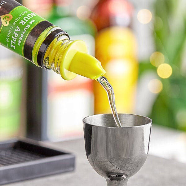 A neon yellow Choice liquor pourer on a bottle of yellow liquid being poured into a glass.