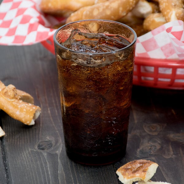 A light amber Cambro plastic tumbler filled with soda and ice next to a basket of pretzels.