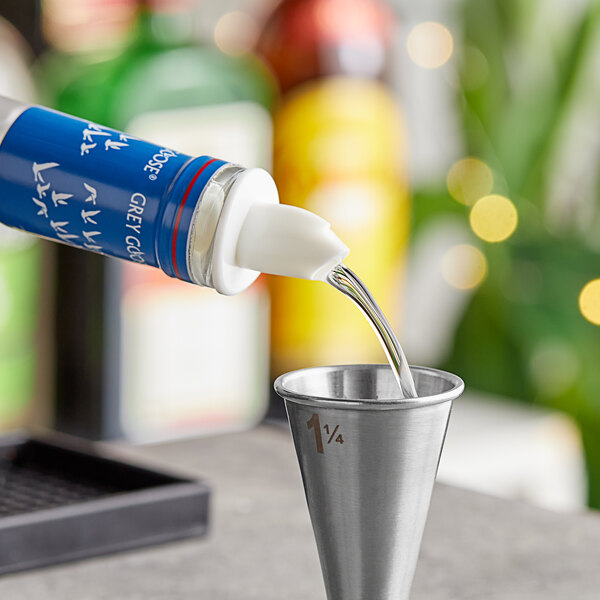 A white metal liquor pourer on a bottle of alcohol pouring into a metal cup.