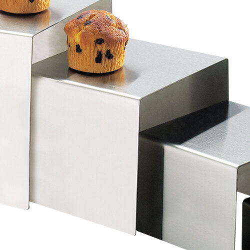 A Cal-Mil stainless steel square riser with muffins on it.
