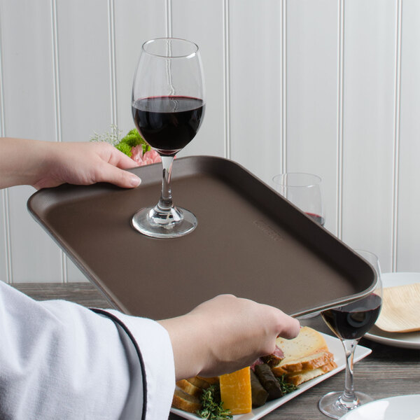 A person holding a Cambro non-skid serving tray with a glass of red wine and food on it.