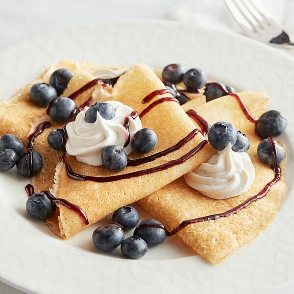 A white plate topped with White Toque thin crepes, blueberries, and whipped cream.