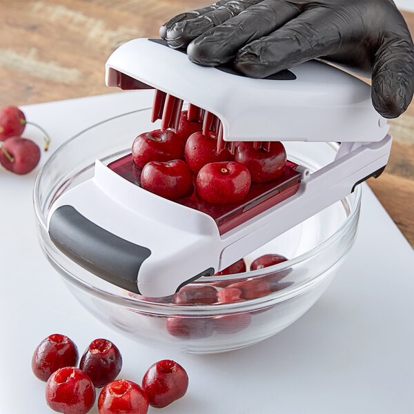 A gloved hand using an OXO cherry pitter to cut cherries.