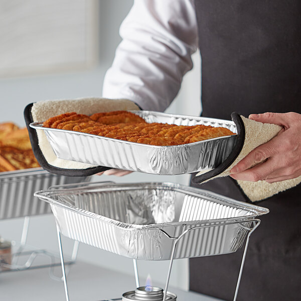 A person holding a tray of food in a Choice aluminum foil steam table pan on a table.