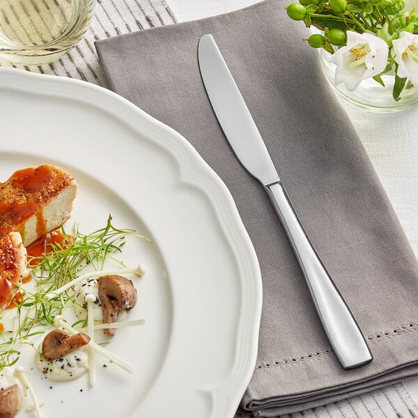 A white plate with a knife on a napkin next to food.