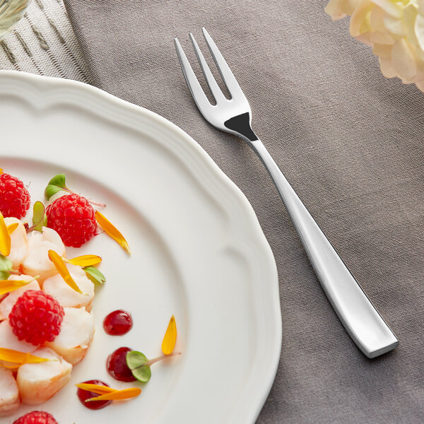 A white plate with a piece of fruit and an Acopa Monte Bianco oyster fork.