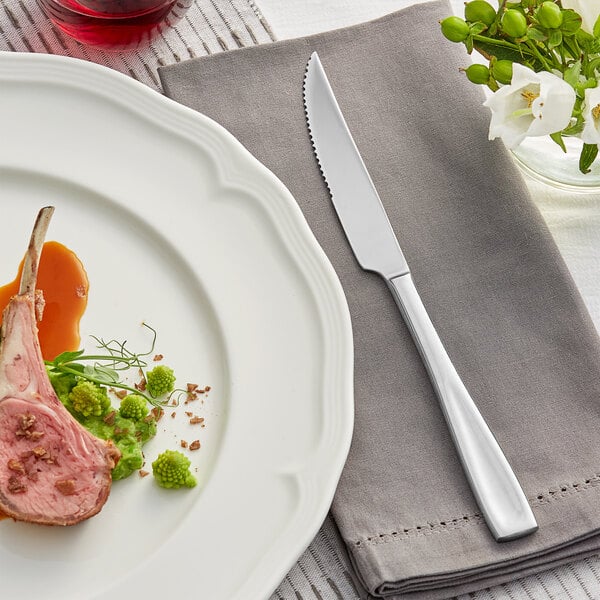 An Acopa stainless steel steak knife on a table with a plate of food and a napkin.
