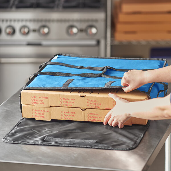 A person putting pizza in a blue Choice insulated delivery bag.