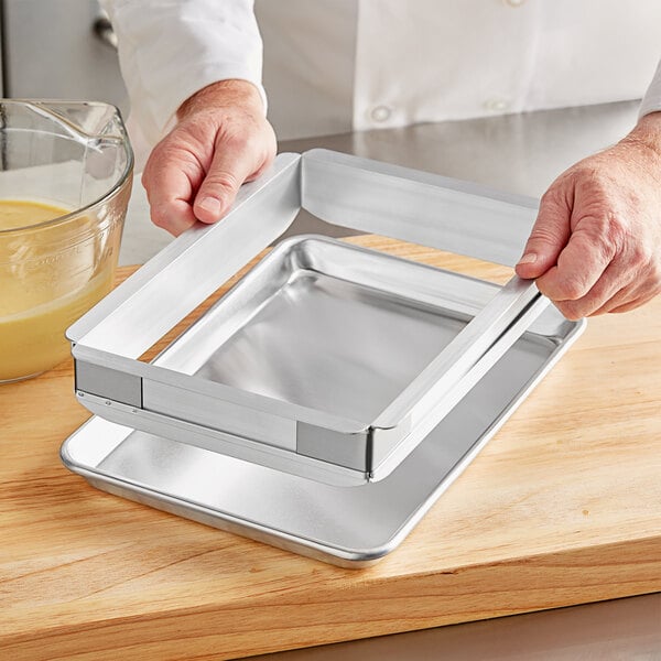 A person holding a Baker's Mark metal sheet cake pan with extender handles.