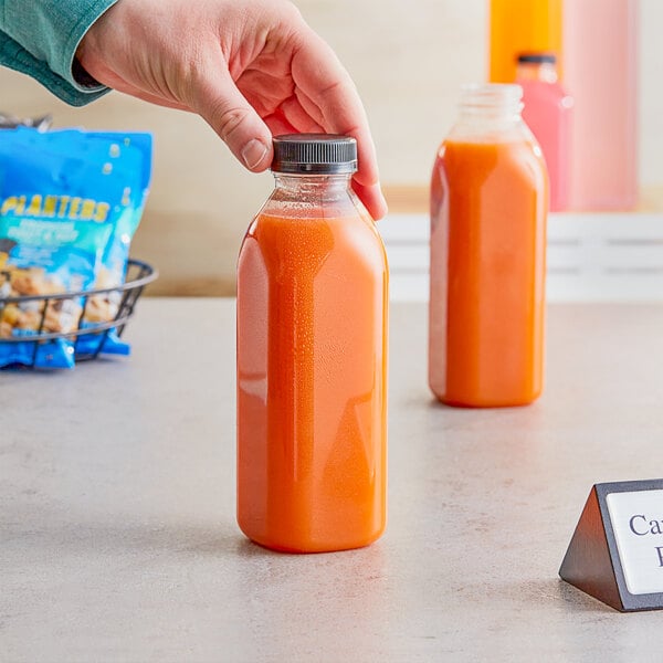 A person holding a 16 oz. square PET clear juice bottle of orange juice.