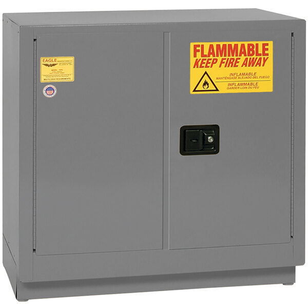 A grey metal Eagle Manufacturing safety cabinet with yellow and red flammable liquid safety signs.