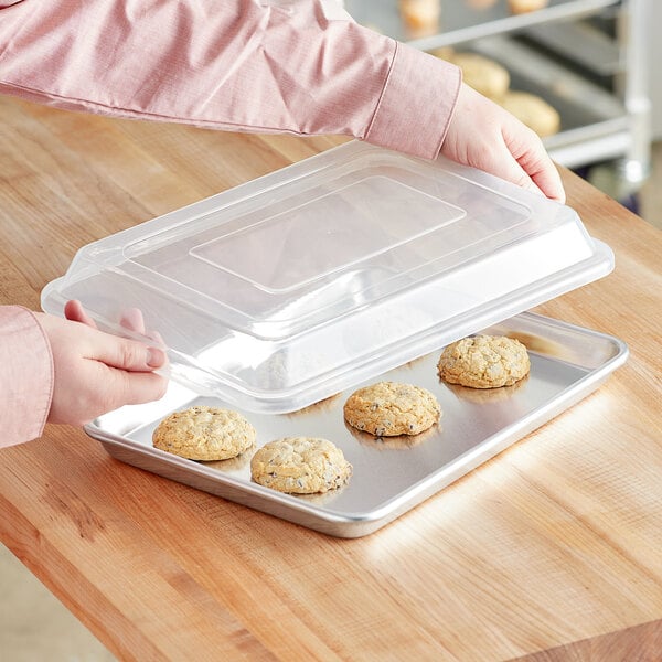 A hand putting cookies in a Choice aluminum sheet pan with a wire rim cover.
