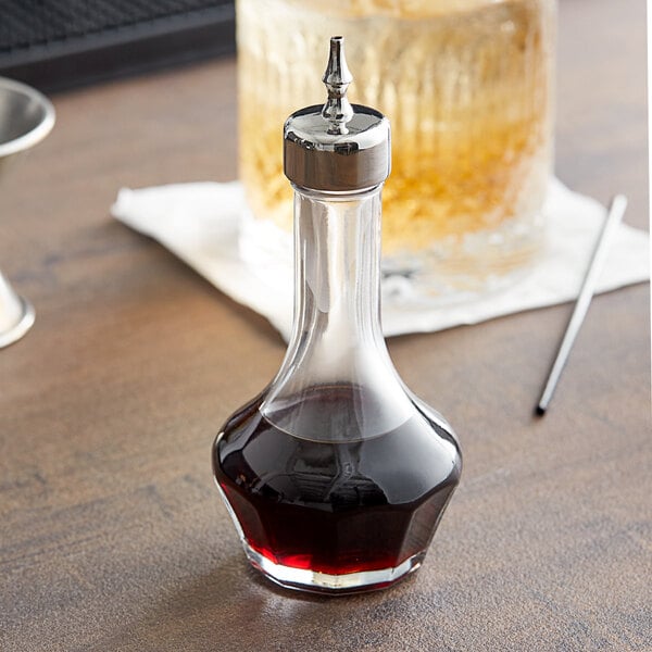 A Barfly glass bitters bottle with a threaded stainless steel top on a table.
