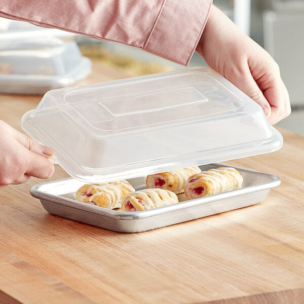 A hand placing a Baker's Mark polypropylene cover on a tray of pastries.