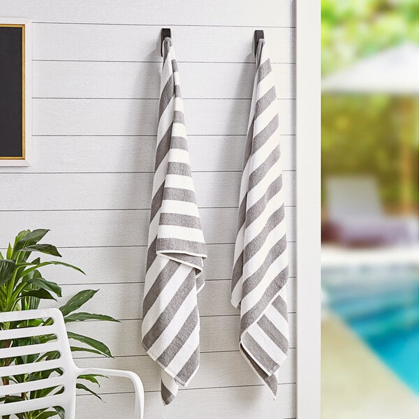 Two Monarch Brands California Cabana gray striped pool towels hanging on a wall.