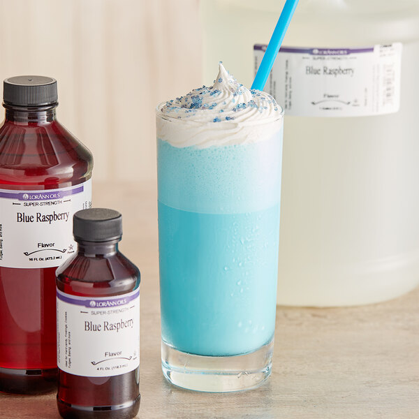 A bottle of LorAnn Oils Blue Raspberry flavoring next to a glass of blue drink with a straw.