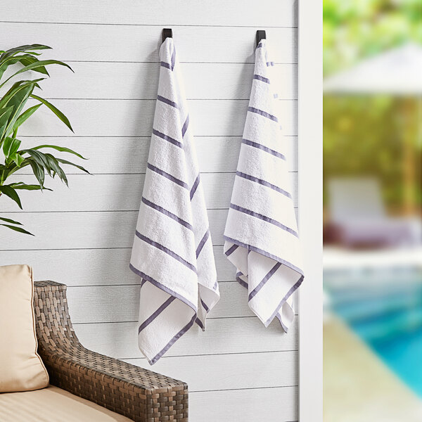 Two Monarch Brands white towels with light gray stripes hanging on a wall.