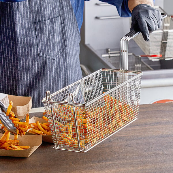 A person in a blue shirt and apron holding a R & V Works fryer basket full of french fries.