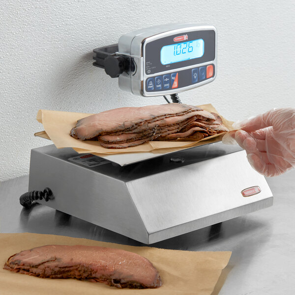 A gloved hand weighing meat on a Tor Rey digital scale.