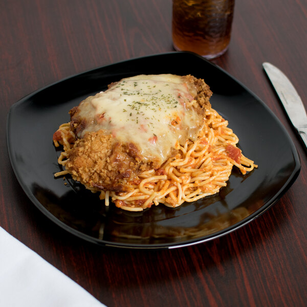 A Carlisle black square melamine plate with spaghetti and chicken on a table.