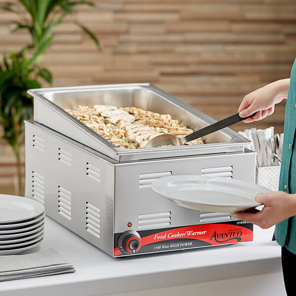 A woman using an Avantco countertop food warmer to serve food from a large pan.