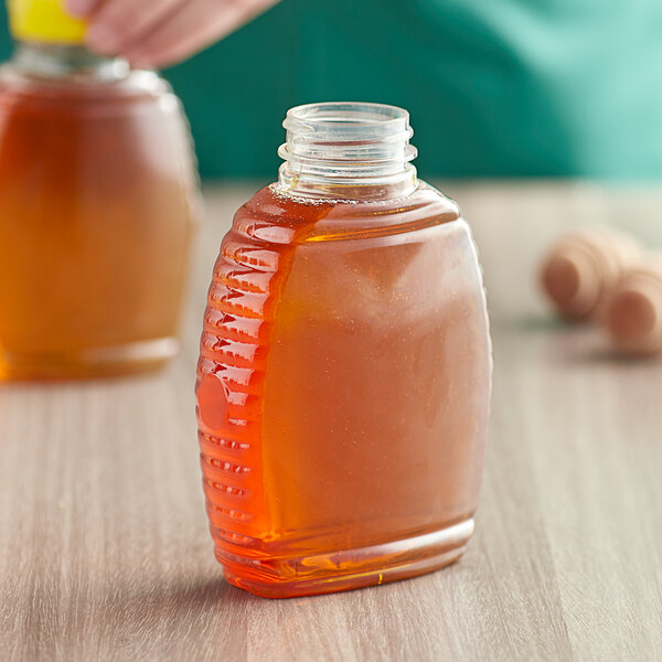 A person pouring honey from a plastic Queenline honey bottle on a table.