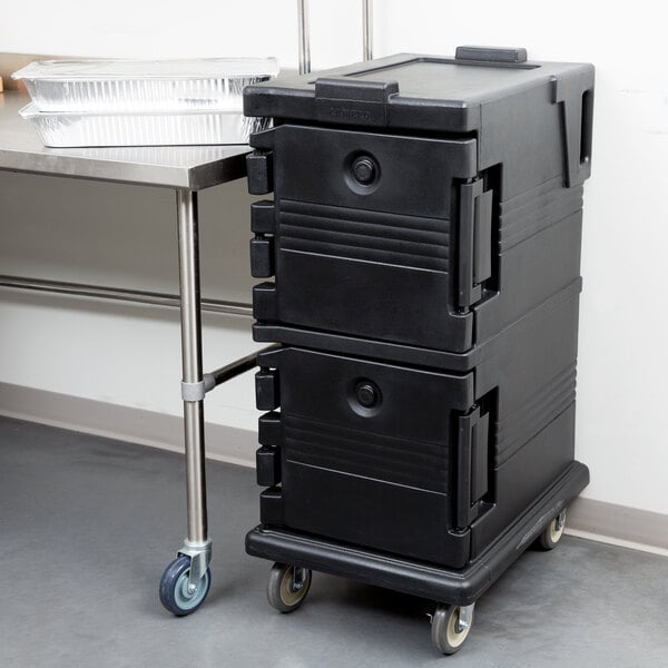 A Cambro black insulated food pan carrier on wheels holding black plastic containers.