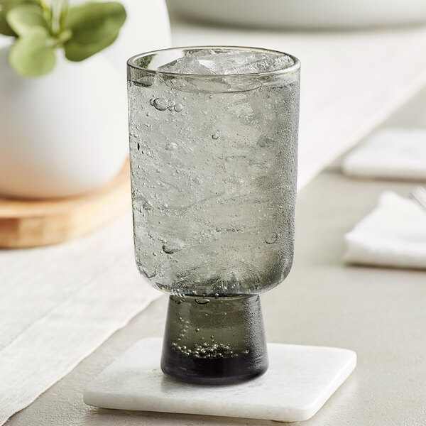 An Acopa gray goblet filled with ice water on a white coaster.