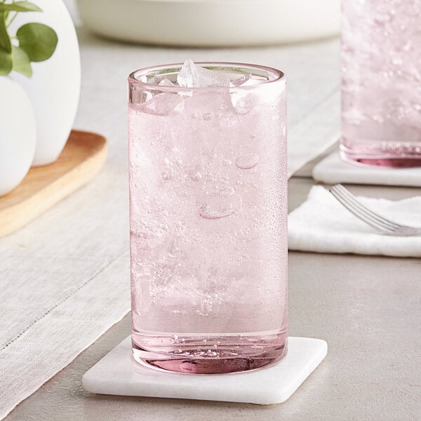 A Mauve Acopa Pangea beverage glass filled with pink liquid and ice on a white coaster.