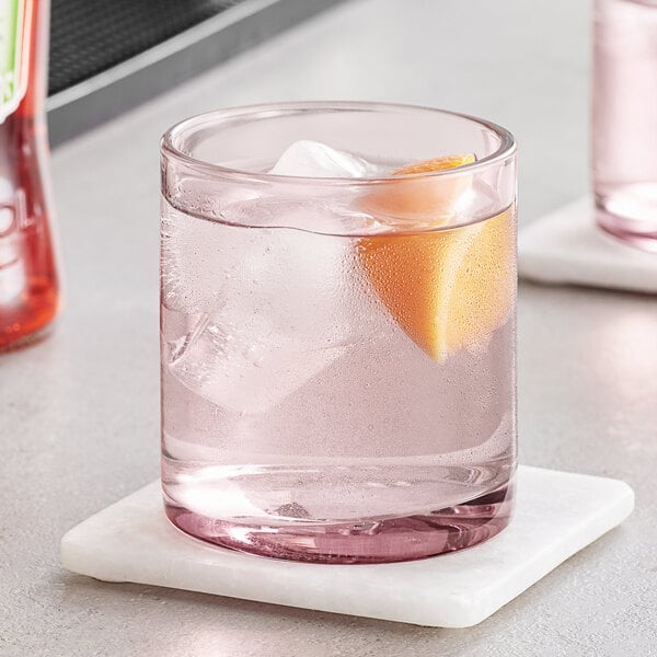 A glass of water with ice and a slice of orange in a mauve Acopa Pangea rocks glass.