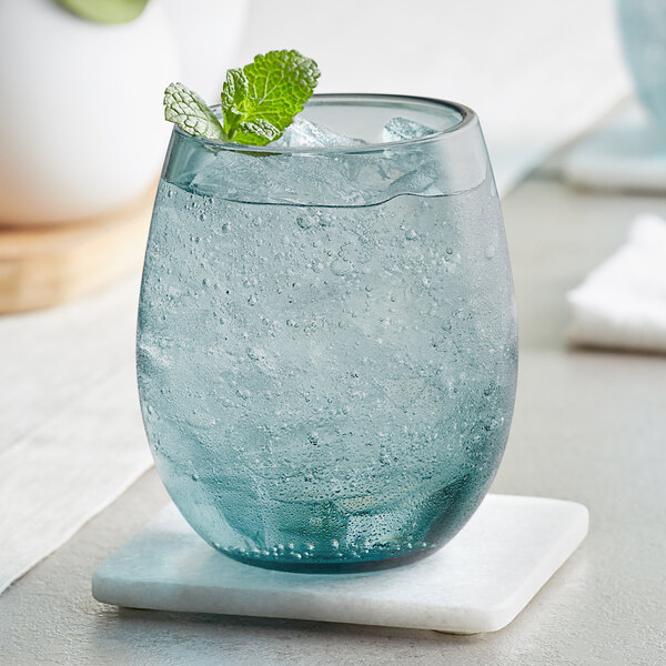 An Acopa blue stemless wine glass filled with water, ice, and mint leaves on a table.