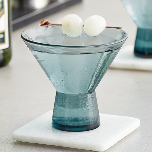 A blue Acopa Pangea martini glass filled with liquid and two round ice balls.