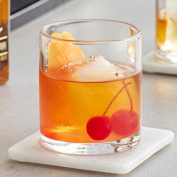 An Acopa Pangea old fashioned glass with orange liquid and cherries.