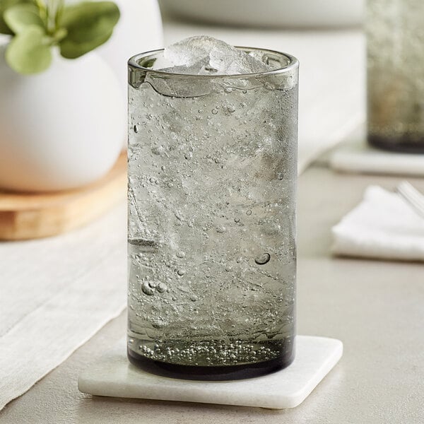 A close-up of an Acopa gray beverage glass with ice water on a coaster.