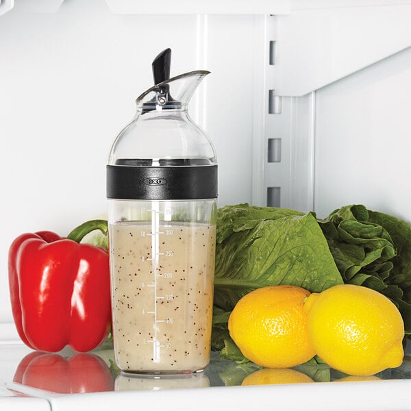 An OXO Good Grips Salad Dressing Shaker filled with salad dressing on a refrigerator shelf.