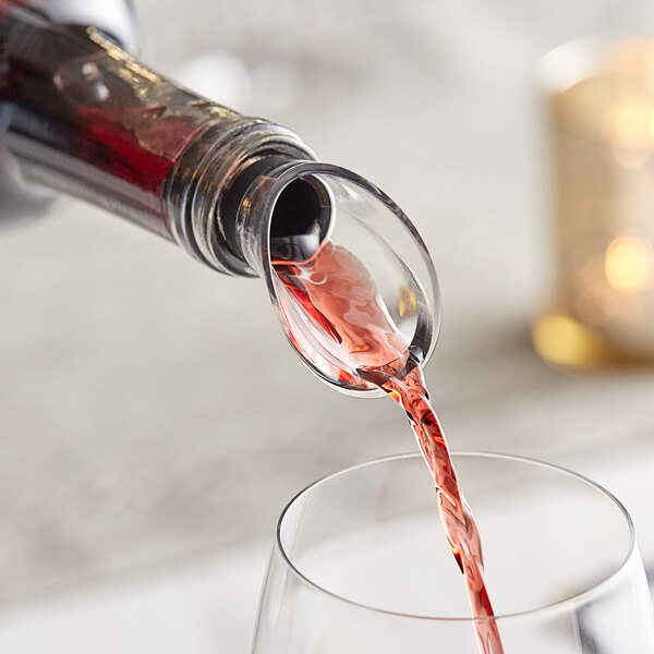 A Vacu Vin crystal wine pourer attached to a wine glass being filled with red wine.