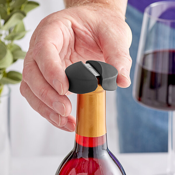 A hand using a Rabbit black foil cutter to open a bottle of wine with a cork stopper.