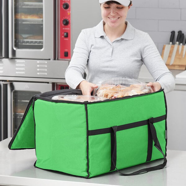 A woman holding a green Choice insulated food delivery bag with food in it.