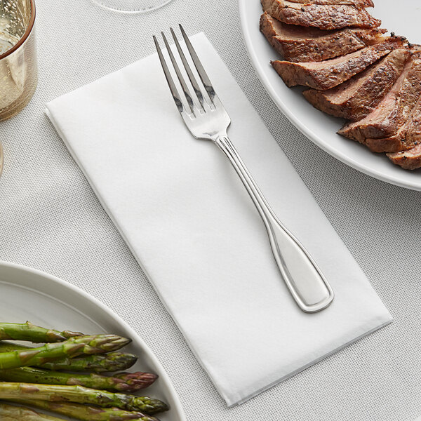 A plate of meat and asparagus on a Hoffmaster white linen-like dinner napkin with a fork.