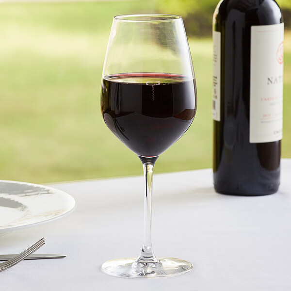 A close-up of a Chef & Sommelier Sequence wine glass with red wine and a bottle of wine on a table.