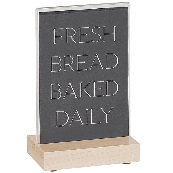 A Cal-Mil maple wood card holder with a black and white sign that says "Fresh Bread Baked Daily" on a counter.