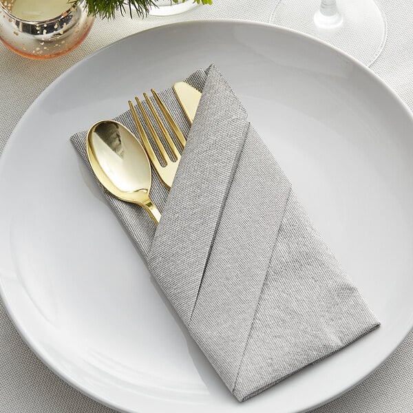 A white plate with a Hoffmaster Natural Onyx dinner napkin and a gold spoon and fork.