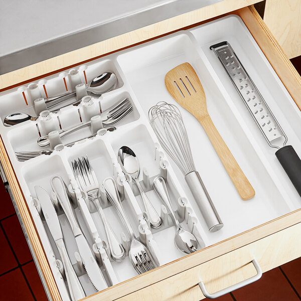 A drawer with white OXO utensil organizer holding wooden spatulas and a whisk.