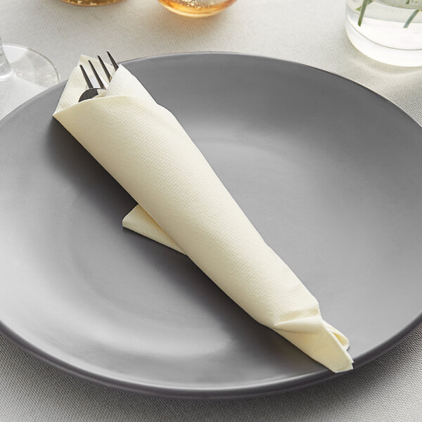 A Hoffmaster ecru linen-like dinner napkin wrapped around a fork and knife on a plate.