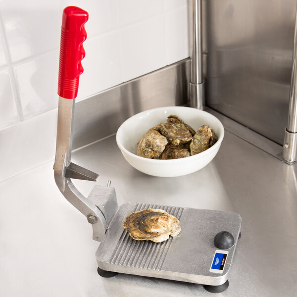 A Vollrath Oyster King stainless steel oyster shucker on a metal cutting board with oysters.